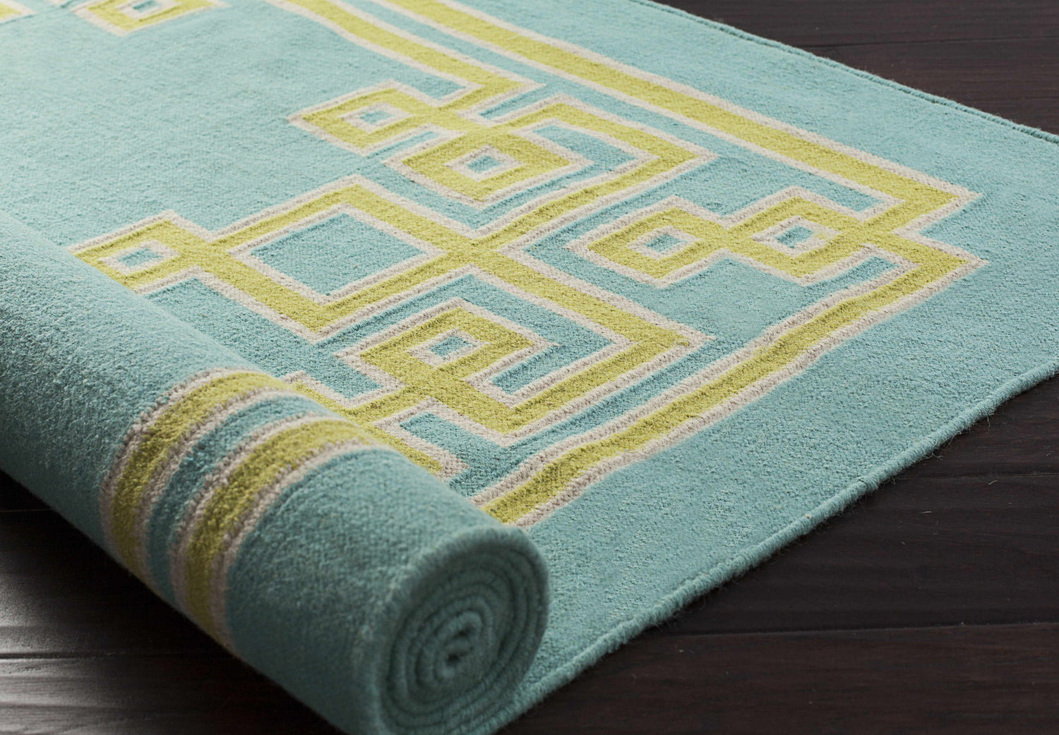 Close-up of a rolled Manitou Area Rug. Aqua wool rug with a geometric light olive and gray pattern. Hand woven texture. Styleshot