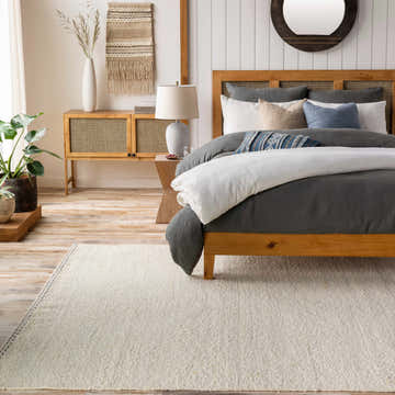 Bedroom scene with a Yaniklar Cream flat woven wool rug, wood bed frame, and neutral decor. Roomscene-Rectangle