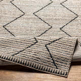 Close-up of the Maonon Area Rug in lambswool and dark gray, featuring a geometric pattern and machine-woven texture. Fold