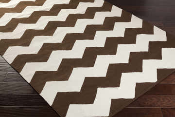 Close-up of the hand woven Masonville Area Rug. Cream and dark brown zig zag pattern on dark wood floor. Corner