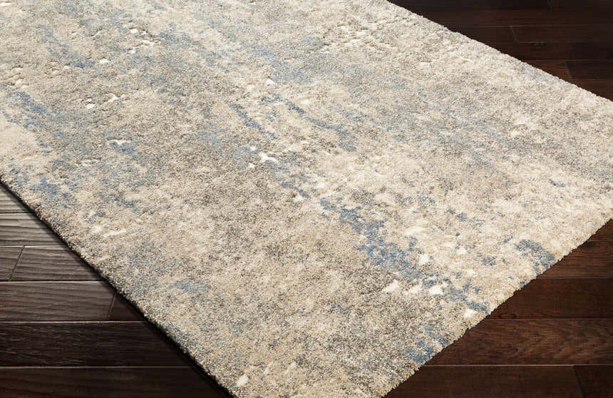 Close-up of Matewan Thick Luxe Rug. Ivory rug with blue and gold abstract pattern and plush texture. Corner