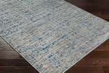 Close-up of the Maungatapere Area Rug, a contemporary rug in cream, gray, light beige, and teal on dark wood flooring. Corner
