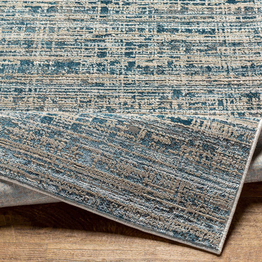 Close up of the Maungatapere Area Rug, a contemporary design in cream, gray, and teal on a wood floor. Fold