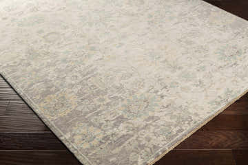 Close-up of the hand-knotted Maybee Area Rug. Wool rug in lavender, light sage, teal, and wheat on dark wood floors. Corner