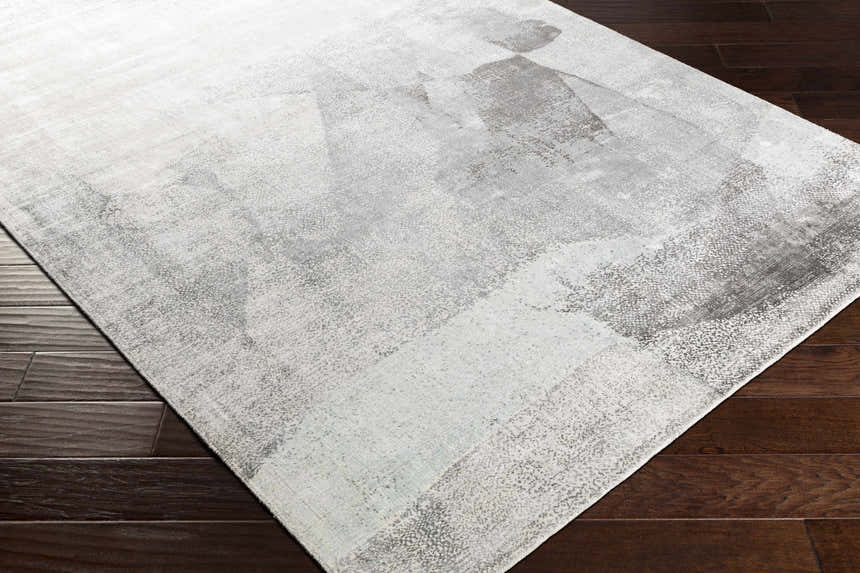 Close-up of the McDowall Viscose Area Rug in black, charcoal, cream, and gray on dark wood flooring. Contemporary hand-loomed design. Corner