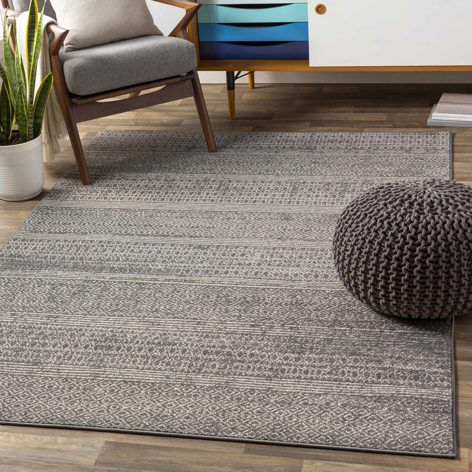 Living room scene with a charcoal Mckinney Area Rug, gray chair, and pouf. The rug features a contemporary geometric pattern. Roomscene-Rectangle