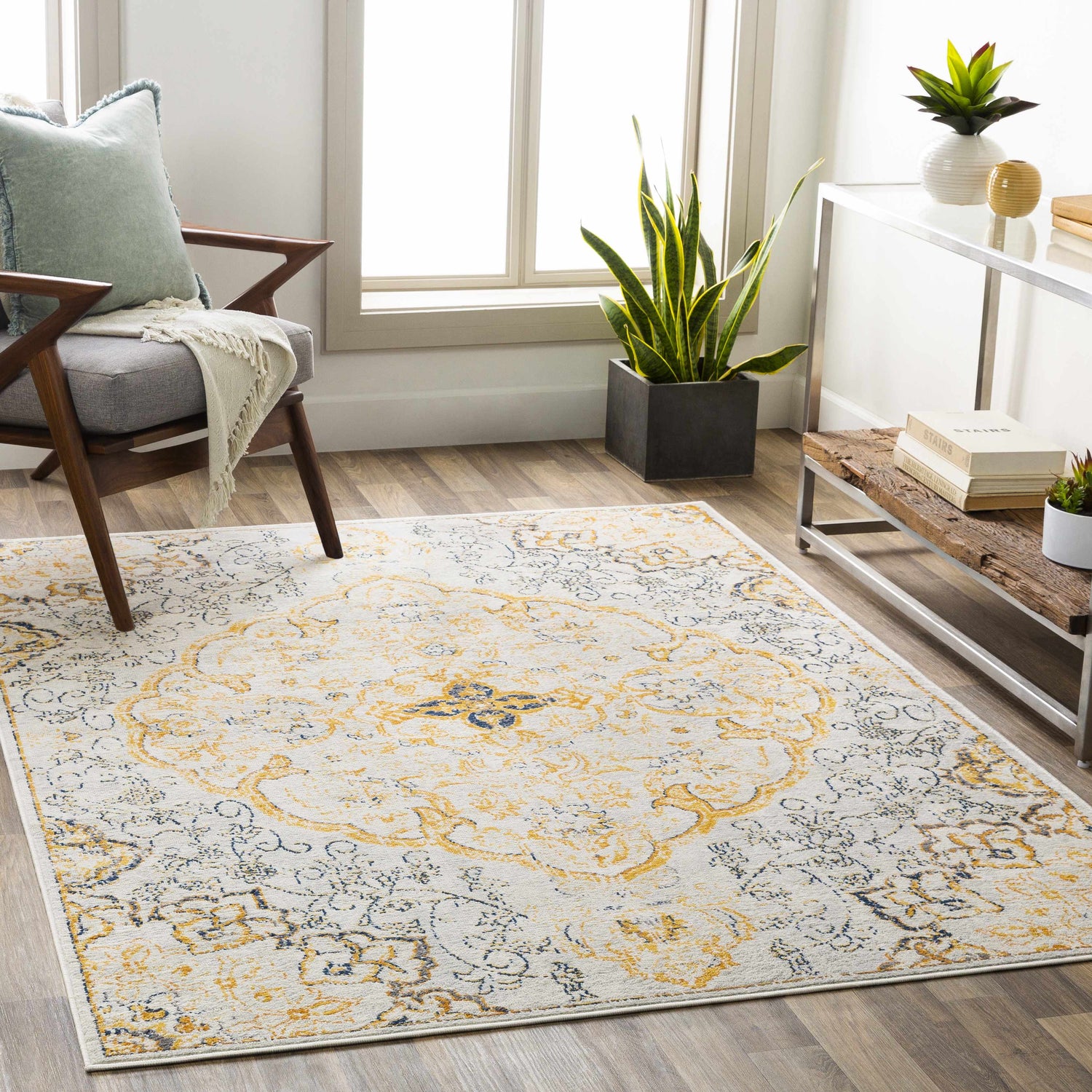 Living room scene with a Mehoopany Area Rug. Bohemian style rug in burnt orange, gray, and navy. Chair, plants, and light wood floors. Roomscene-Rectangle