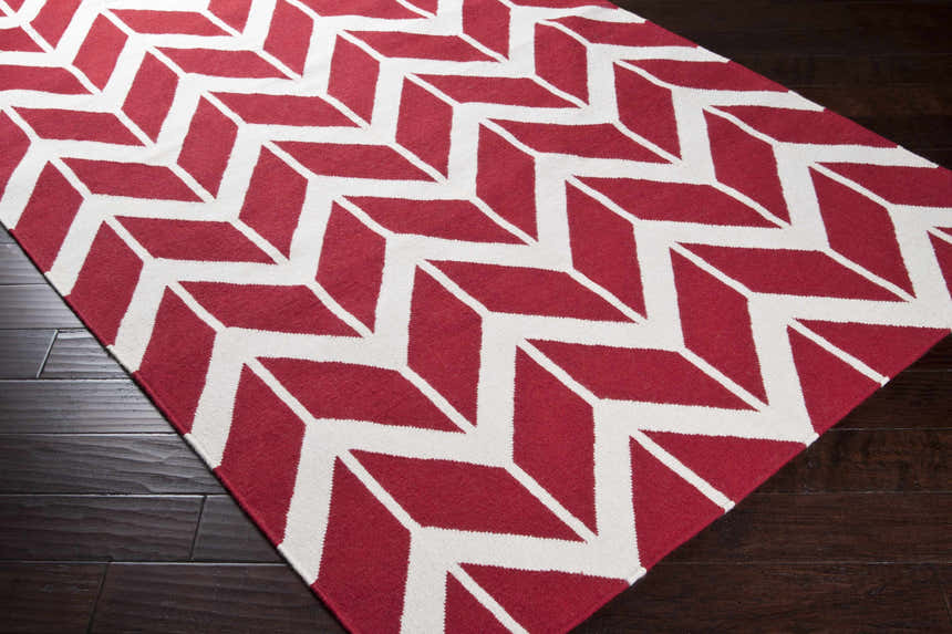 Close-up of the hand-woven Melbeta Area Rug. Red and white geometric pattern on a wool rug. Corner