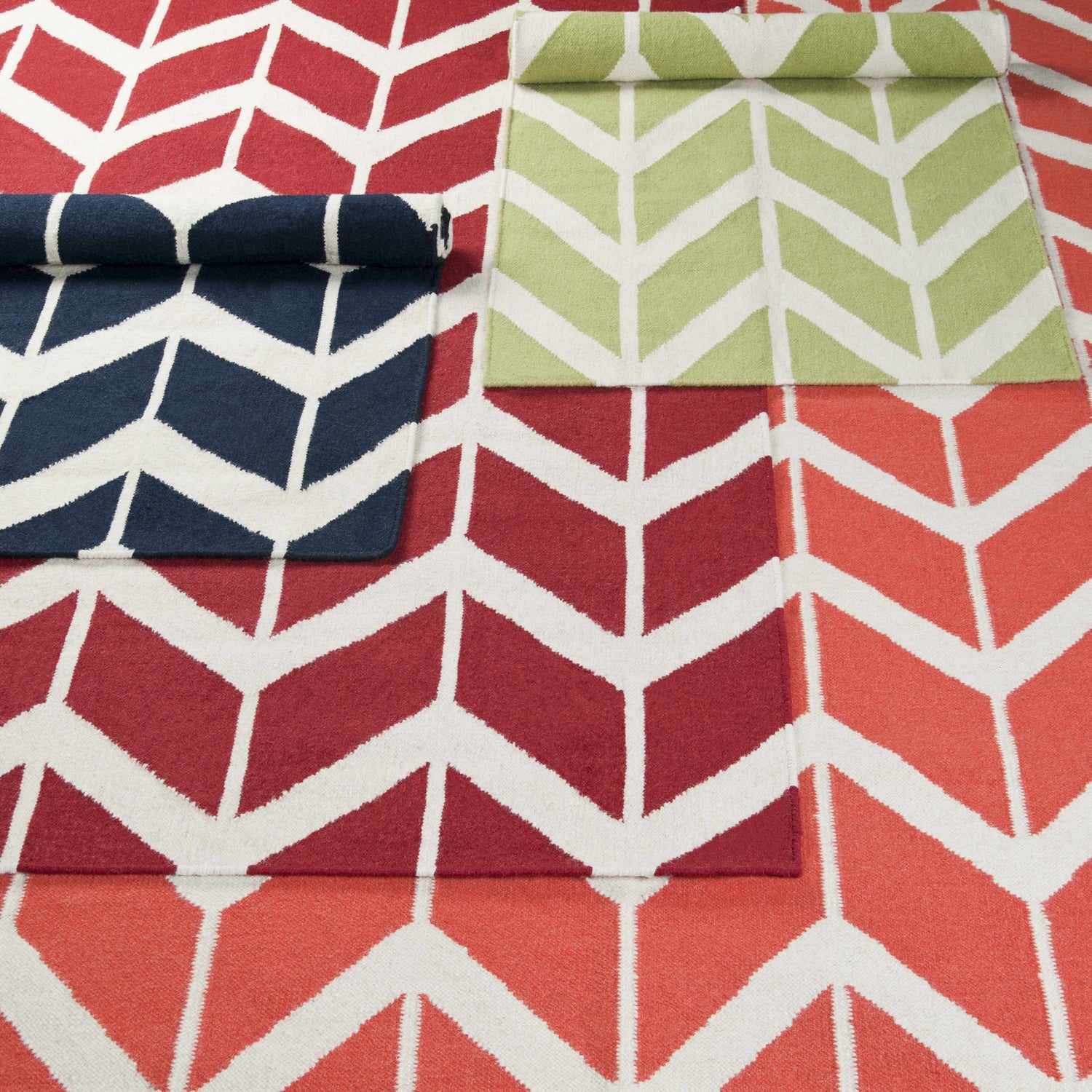 Melbeta Area Rug close-up: wool rug with a geometric chevron pattern in red, coral, navy, and green on white. Styleshot