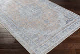 Close-up of the Mianay Washable Area Rug showing its beige, blue, and light gray vintage-style pattern on dark wood flooring. Corner