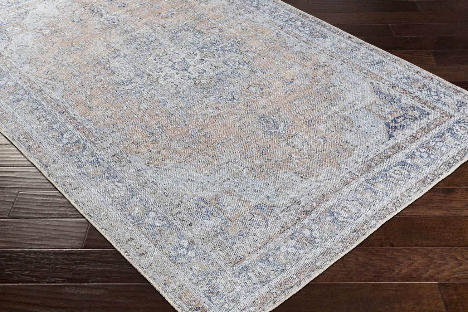 Close-up of the Mianay Washable Area Rug showing its beige, blue, and light gray vintage-style pattern on dark wood flooring. Corner