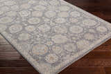 Close-up of the Mimarsinan Thick Luxe Statement Rug. Oriental floral pattern in gray, beige, and brown on dark wood floor. Corner