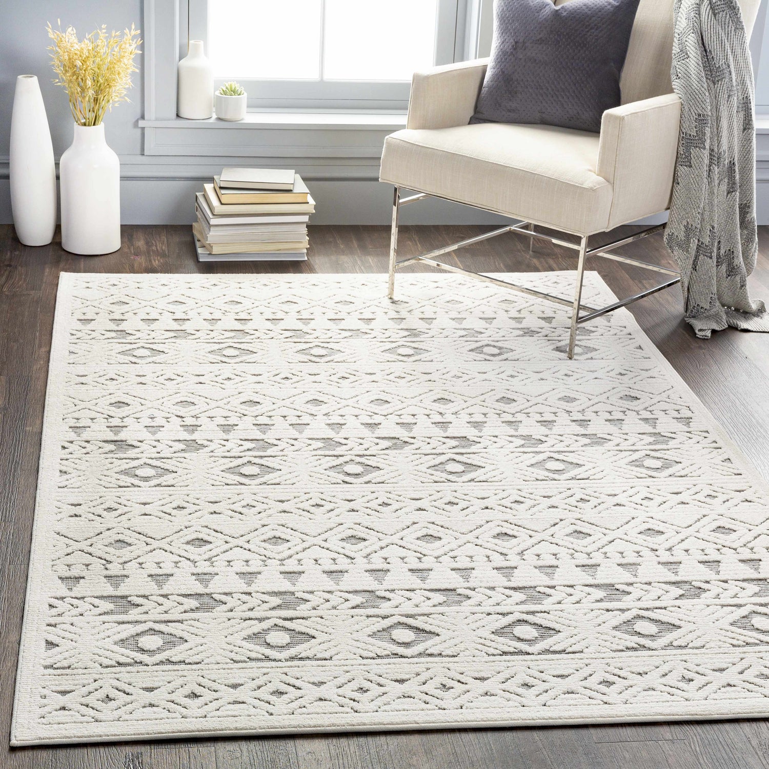 Living room scene with a light beige chair and the Mirani 3D Outdoor Area Rug in charcoal and light beige. Roomscene-Rectangle