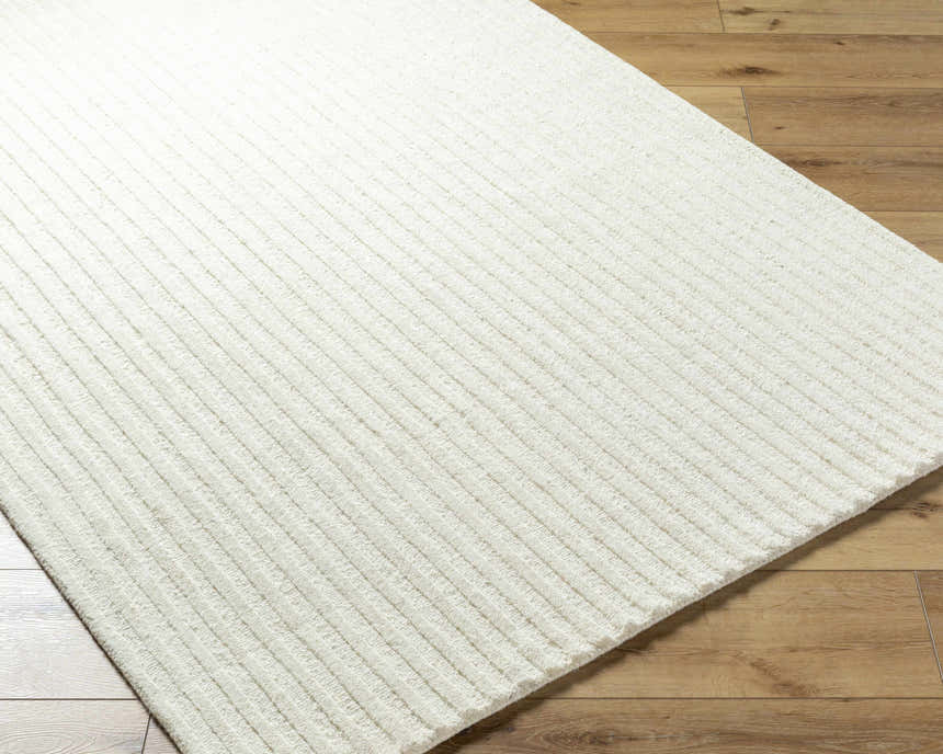 Close-up of the hand-tufted Missa Cream Area Rug showing its subtle striped design and 100% wool texture on wood floor. Corner