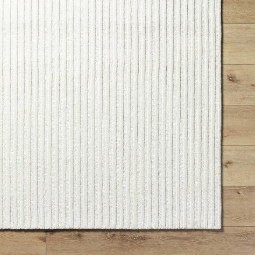 Close up of the cream Missa Area Rug showing its textured, vertical striped design on wood flooring. Corner