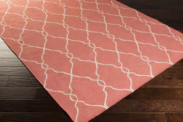 Close-up of the Melcher Area Rug in oatmeal and rose, featuring a geometric trellis pattern on dark wood floors. Corner