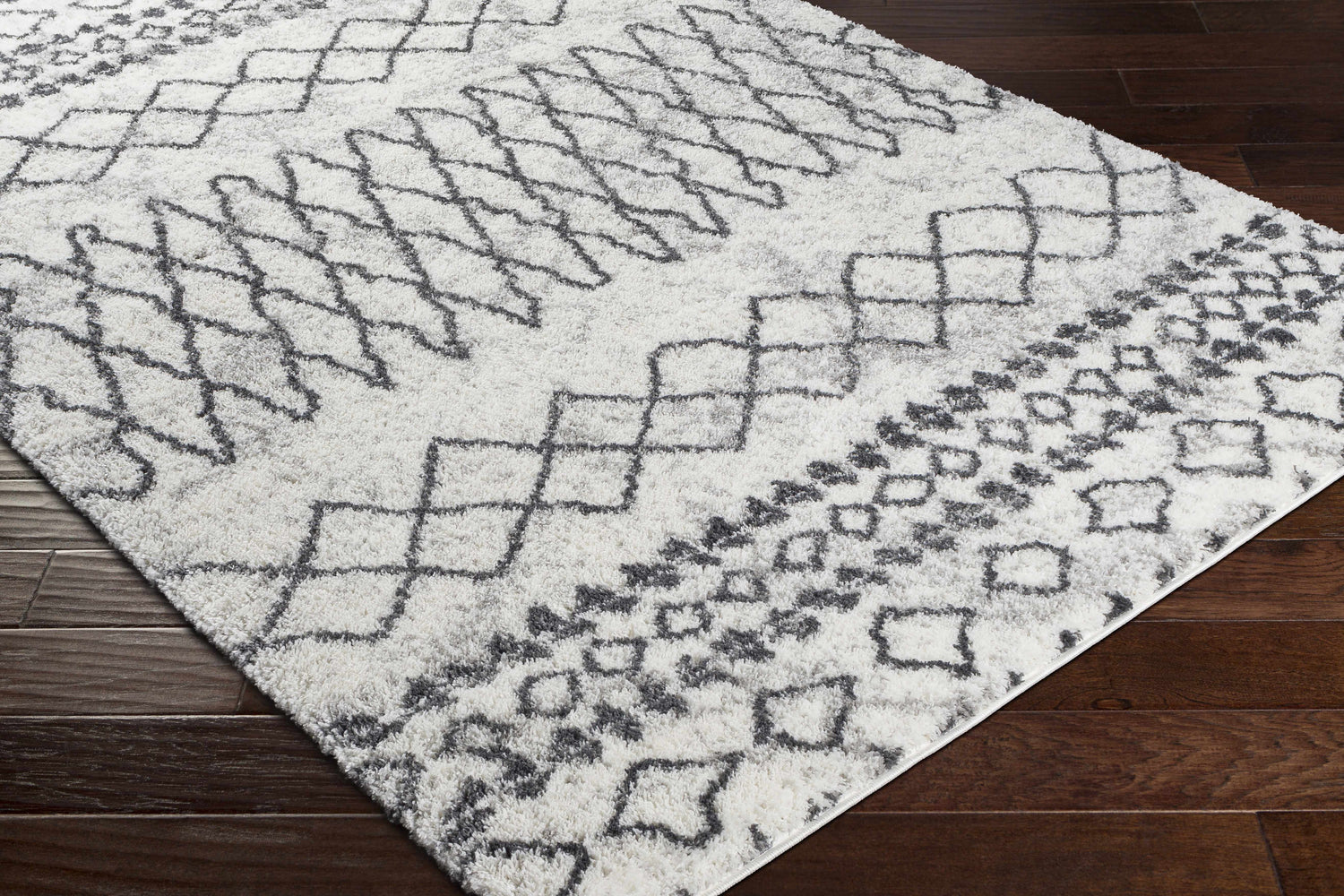 Close-up of the Moulden Area Rug. Shag rug with a geometric charcoal and cream pattern on dark wood floors. Corner