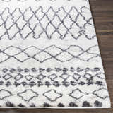 Close-up of the Moulden Area Rug. Cream shag rug with charcoal geometric diamond pattern on dark wood floor. Front