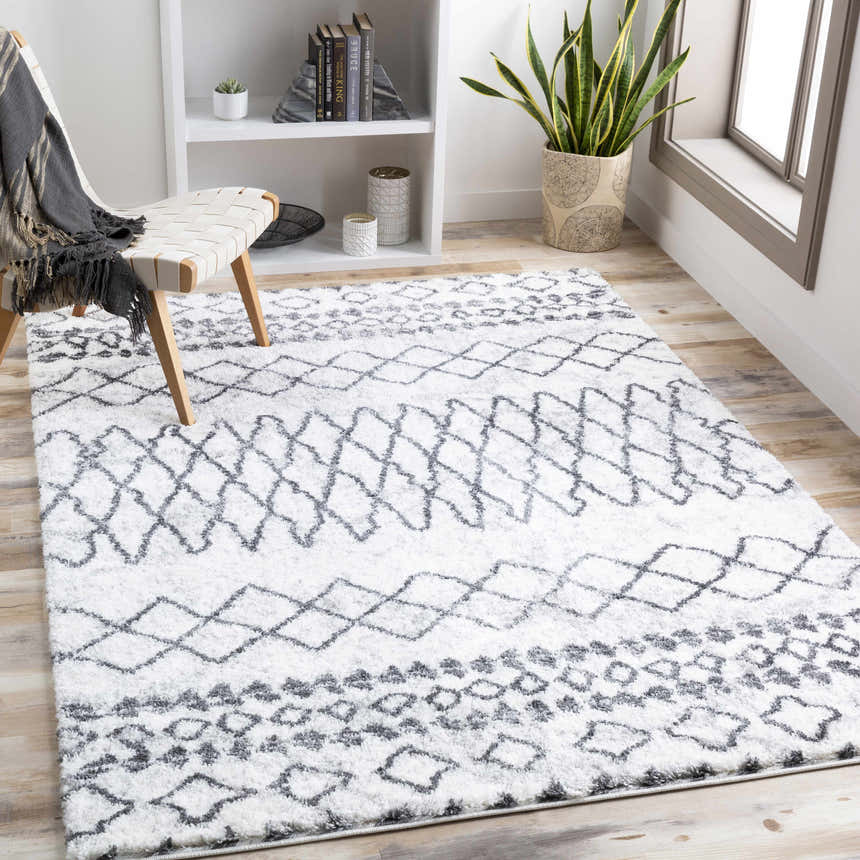 Light and airy room scene with a charcoal and cream Moulden Area Rug, chair with throw, and white bookshelf. Roomscene-Rectangle