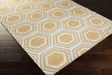 Close-up of Millstone Area Rug. Hand-woven wool rug with light beige, sage, and tan geometric hexagon pattern. Corner