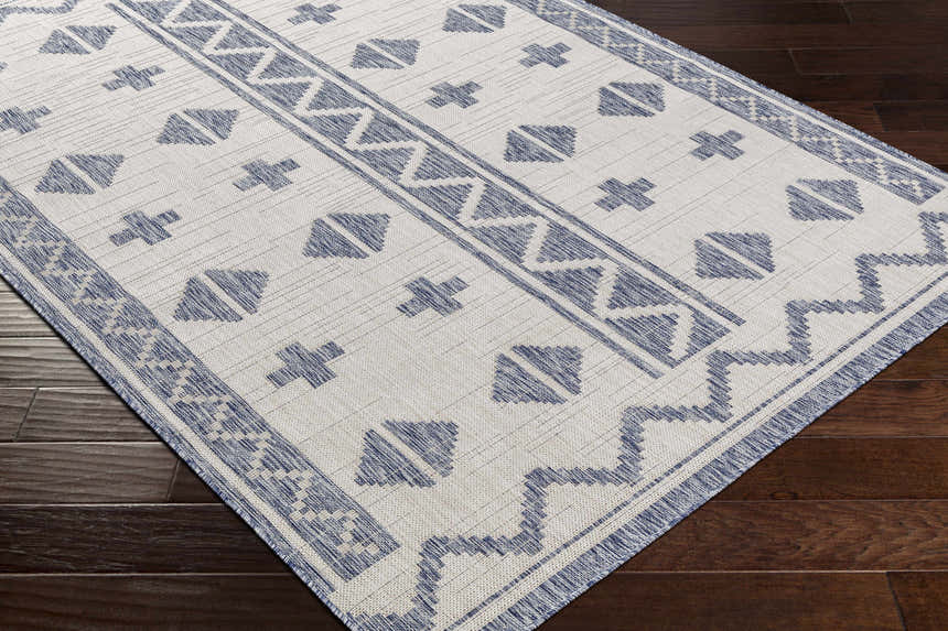 Close-up of Mangoso Gray Area Rug showing blue geometric pattern on off-white background, machine woven texture. Corner