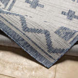 Close-up of the Mangoso Gray Area Rug showing its blue geometric pattern and woven texture on a beige tile floor. Fold