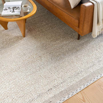 Living room scene with a tan leather sofa and Manatal Flat Woven Wool Rug in beige, charcoal, and cream. Roomscene-Rectangle