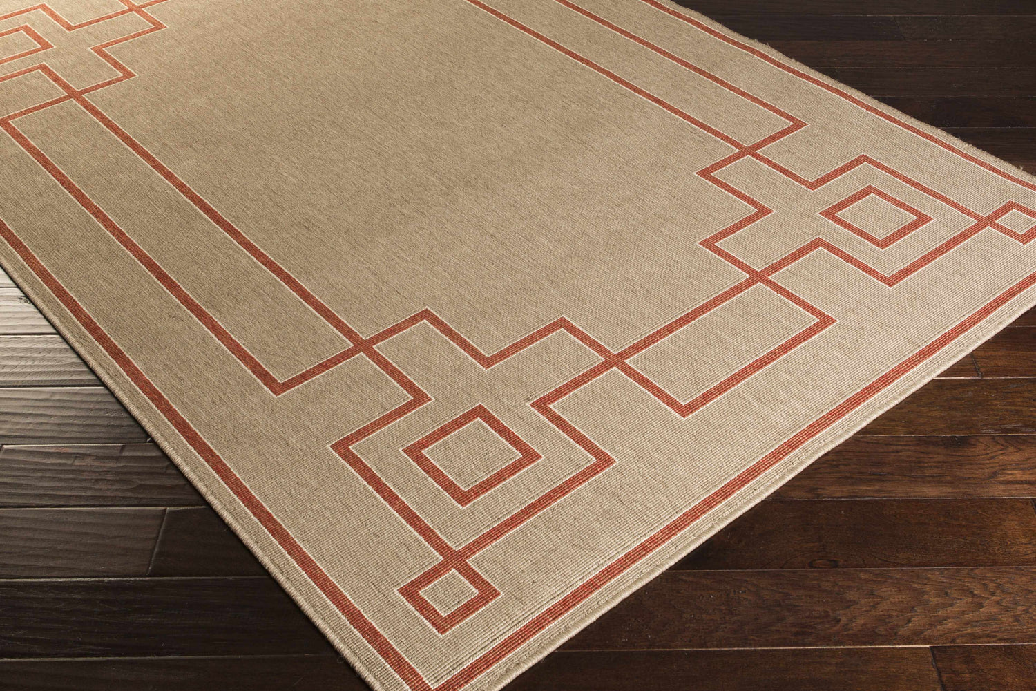 Close-up of the Moffett Area Rug, showcasing a brick red geometric border on a light beige olefin rug. Corner