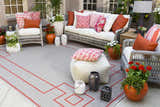Brick red Moffett Area Rug on a patio with wicker furniture, colorful pillows, and potted plants. Styleshot