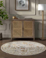Living room scene with a round Mogul Luxe Oushak Rug in cream, brick red, denim, and tan under a cabinet. Roomscene-Round