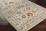 Close-up of the Mogul Luxe Oushak Rug. Cream rug with brick red, denim, mustard, and olive floral pattern on dark wood floor. Corner