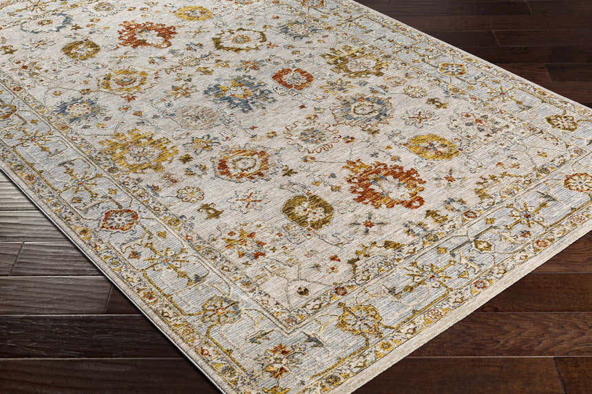 Close-up of the Mogul Luxe Oushak Rug. Cream rug with brick red, denim, mustard, and olive floral pattern on dark wood floor. Corner
