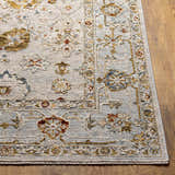 Close-up of the Mogul Luxe Oushak Rug. Features brick red, cream, denim, mustard, and tan floral pattern on a light gray background. Front