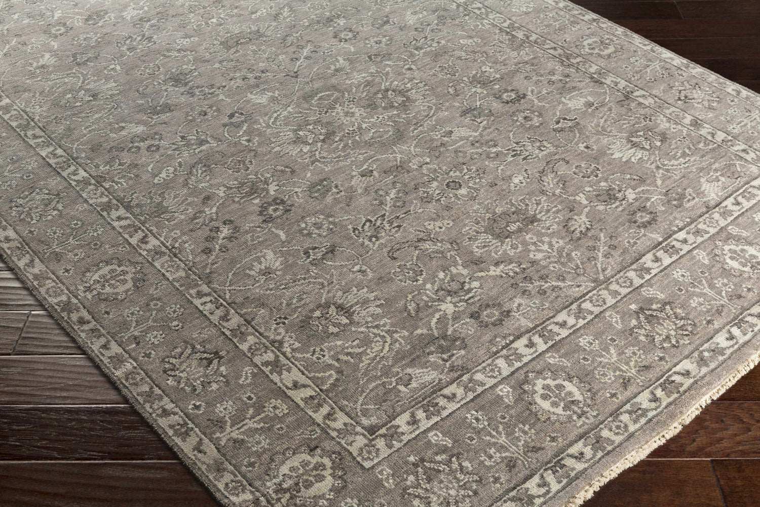 Close-up of the Momeyer Area Rug. Hand-knotted wool rug in dark brown, light gray, and taupe with a traditional floral pattern. Corner