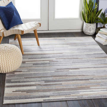 Entryway scene with a Monkland Area Rug in charcoal, gray, light gray, tan, and white. Modern chair and pouf. Roomscene-Rectangle