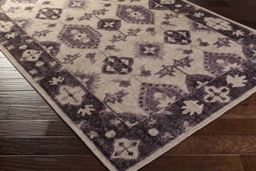 Close up of the hand knotted Monon Area Carpet in dark plum, lavender, and medium gray on dark wood floors. Corner