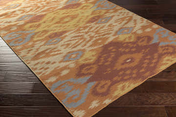 Close-up of the Monson Area Rug, a hand-woven wool rug with a contemporary ikat pattern in brick red, camel, and gray. Corner