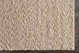 Close-up of the hand woven Monticello Carpet. Light beige wool rug with a chunky, textured weave on dark brown wood floor. Corner