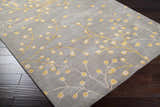 Close-up of the Elsu Mustard Wool Area Rug. Charcoal rug with a mustard and taupe floral branch pattern. Hand-tufted texture. Corner