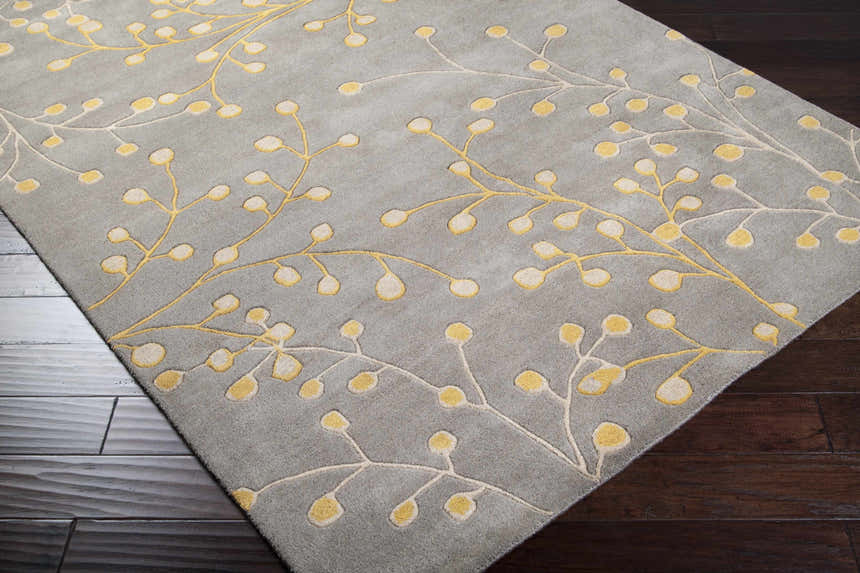 Close-up of the Elsu Mustard Wool Area Rug. Charcoal rug with a mustard and taupe floral branch pattern. Hand-tufted texture. Corner