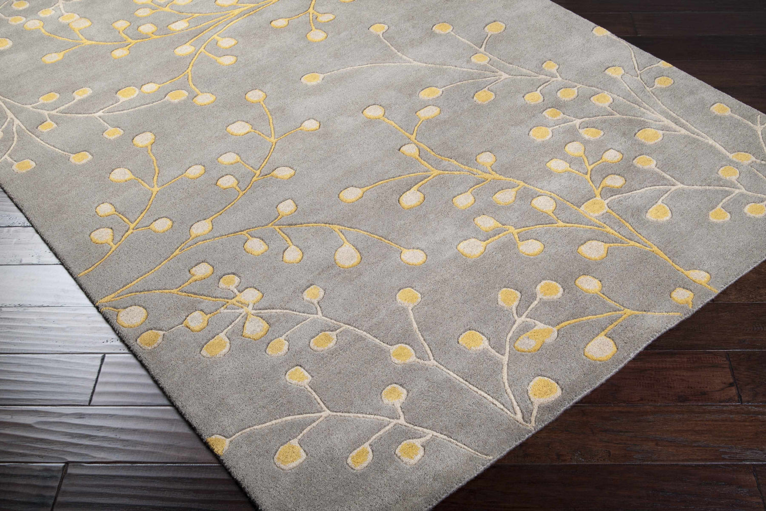 Close-up of the Elsu Mustard Wool Area Rug. Charcoal rug with a mustard and taupe floral branch pattern. Hand-tufted texture. Corner