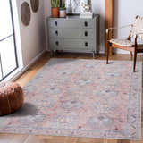 Living room scene with a Morcott Peach Washable Area Rug, gray dresser, leather pouf, and woven chair on a wood floor. Roomscene-Rectangle