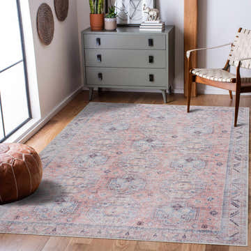 Living room scene with a Morcott Peach Washable Area Rug, gray dresser, leather pouf, and woven chair on a wood floor. Roomscene-Rectangle