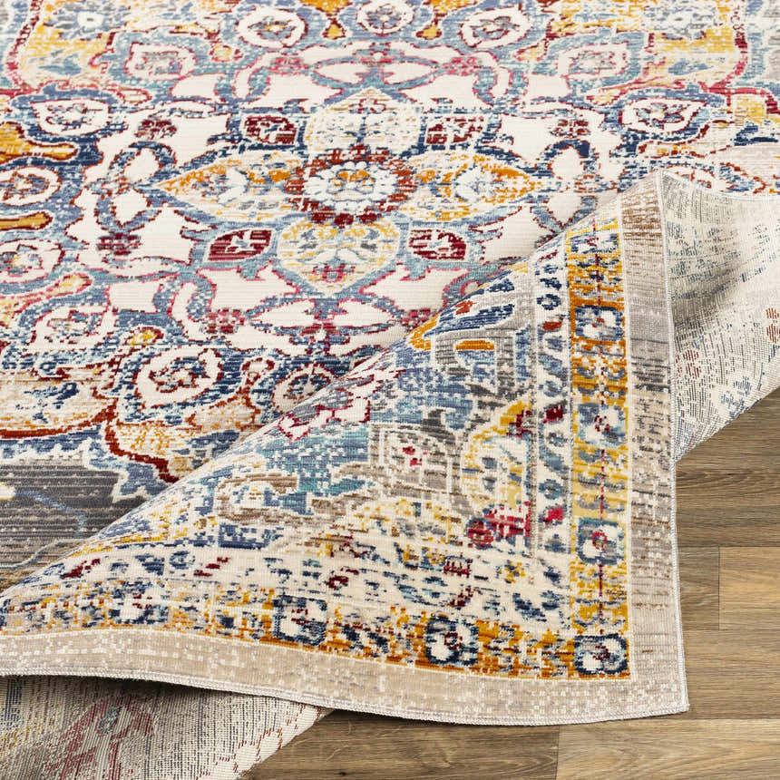 Close-up of the Mortdale Area Rug. Bohemian style rug in aqua, burgundy, camel, denim, gray, mustard, purple, and white. Fold