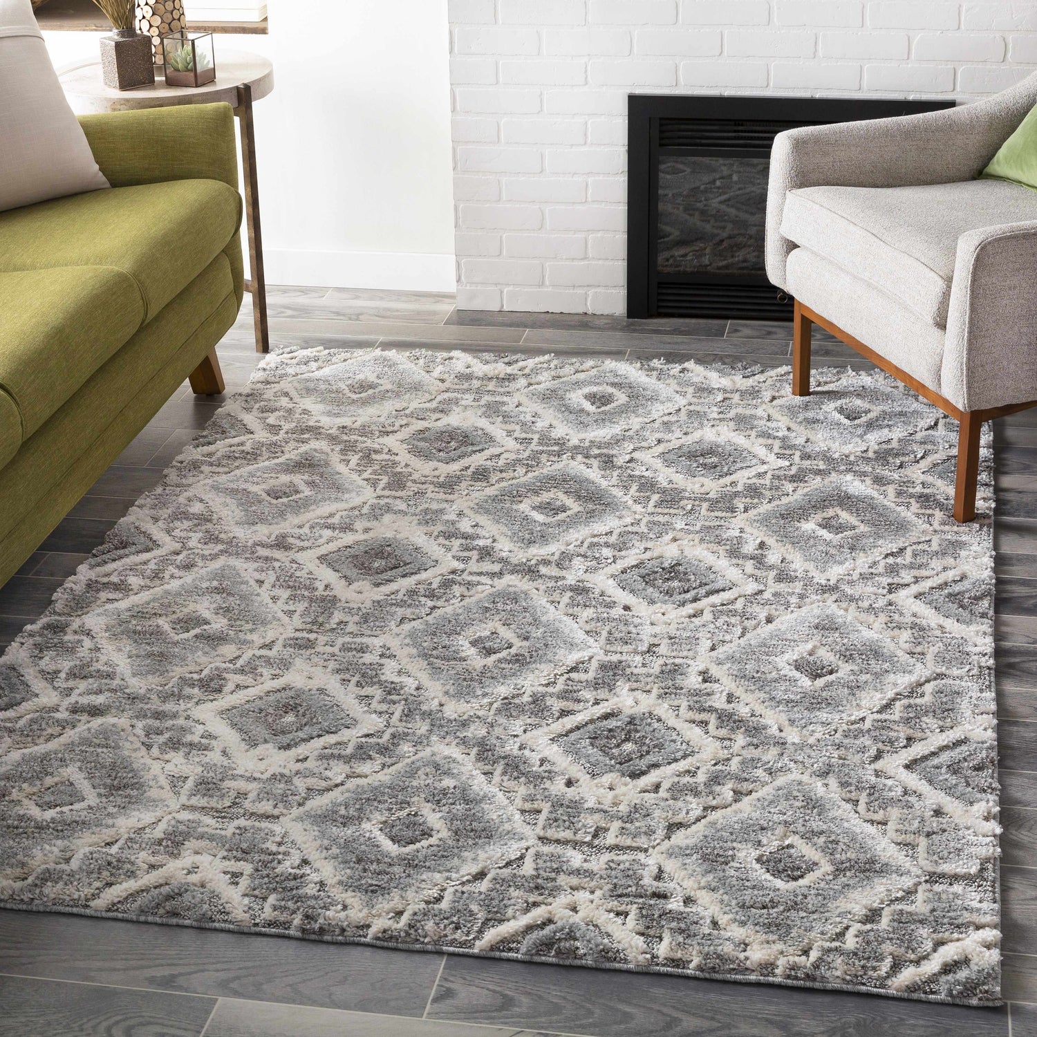 Living room scene with a Moruya Area Rug in beige, charcoal, and cream, styled with a green sofa and gray armchair. Roomscene-Rectangle