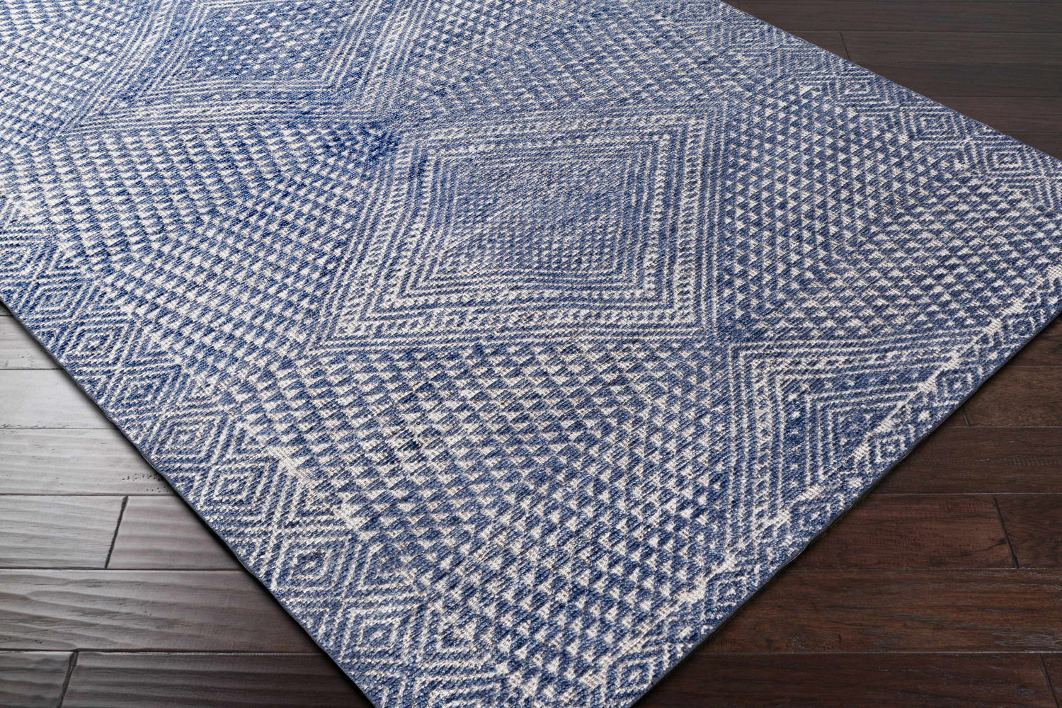 Close-up of the Moyne Area Rug, showcasing its blue and white geometric diamond pattern and hand-knotted texture. Corner