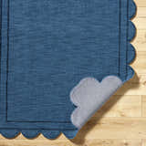Close-up of the hand-loomed Uhuro Blue Geometric Area Rug with a unique scalloped edge on light wood flooring. Fold