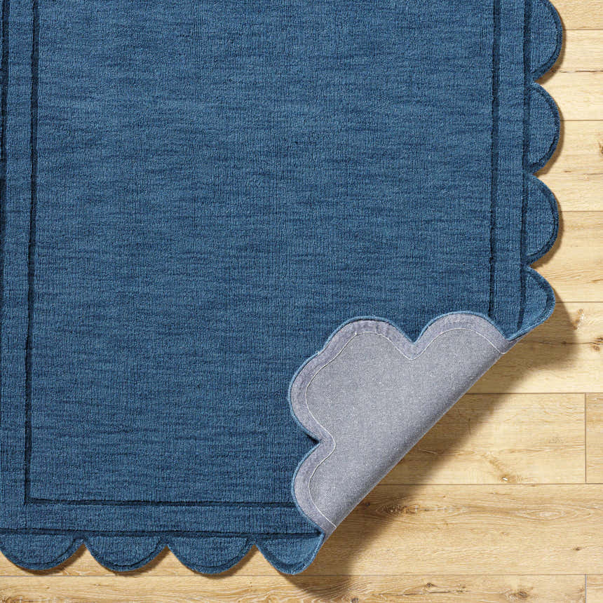 Close-up of the hand-loomed Uhuro Blue Geometric Area Rug with a unique scalloped edge on light wood flooring. Fold