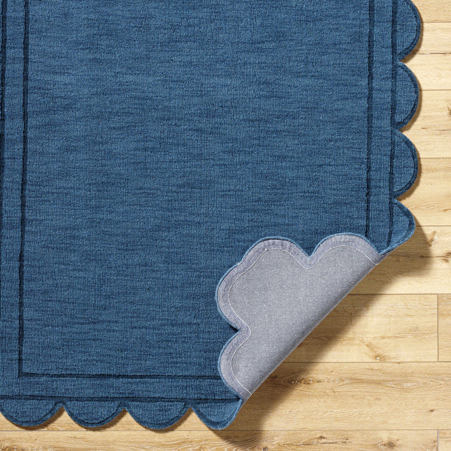 Close-up of the hand-loomed Uhuro Blue Geometric Area Rug with a unique scalloped edge on light wood flooring. Fold