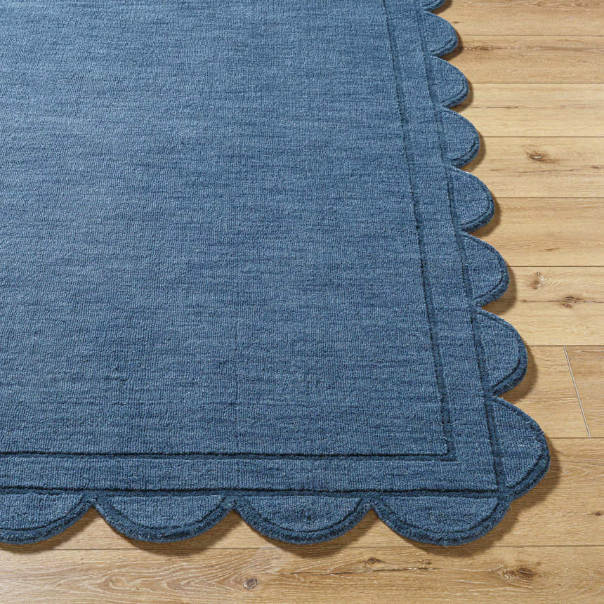 Close-up of the hand-loomed Uhuro Blue Geometric Area Rug showing its wool texture and scalloped edge detail on wood floor. Front